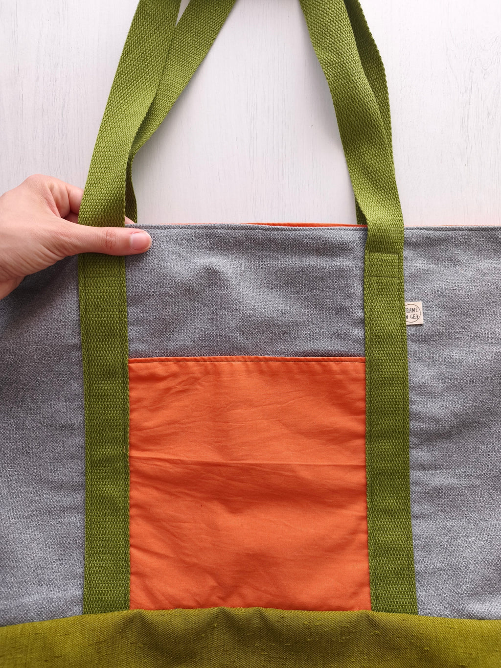 Borsa capiente grigia con tasca arancione, cighie verdi e base della borsa verde