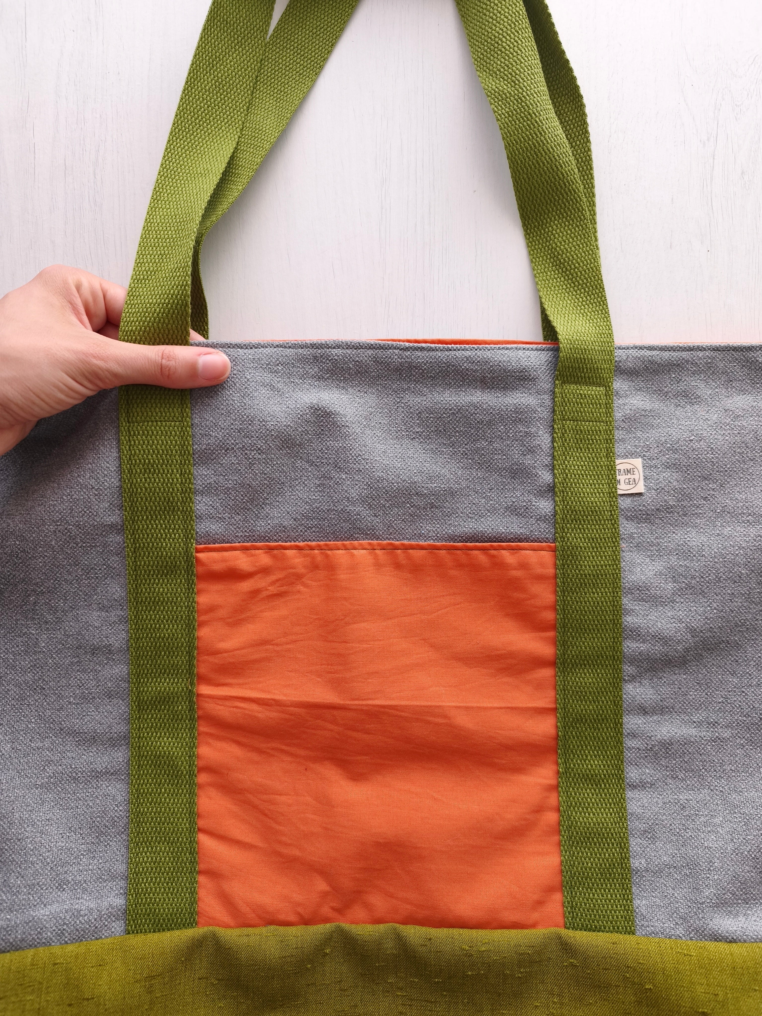 Borsa capiente grigia con tasca arancione, cighie verdi e base della borsa verde