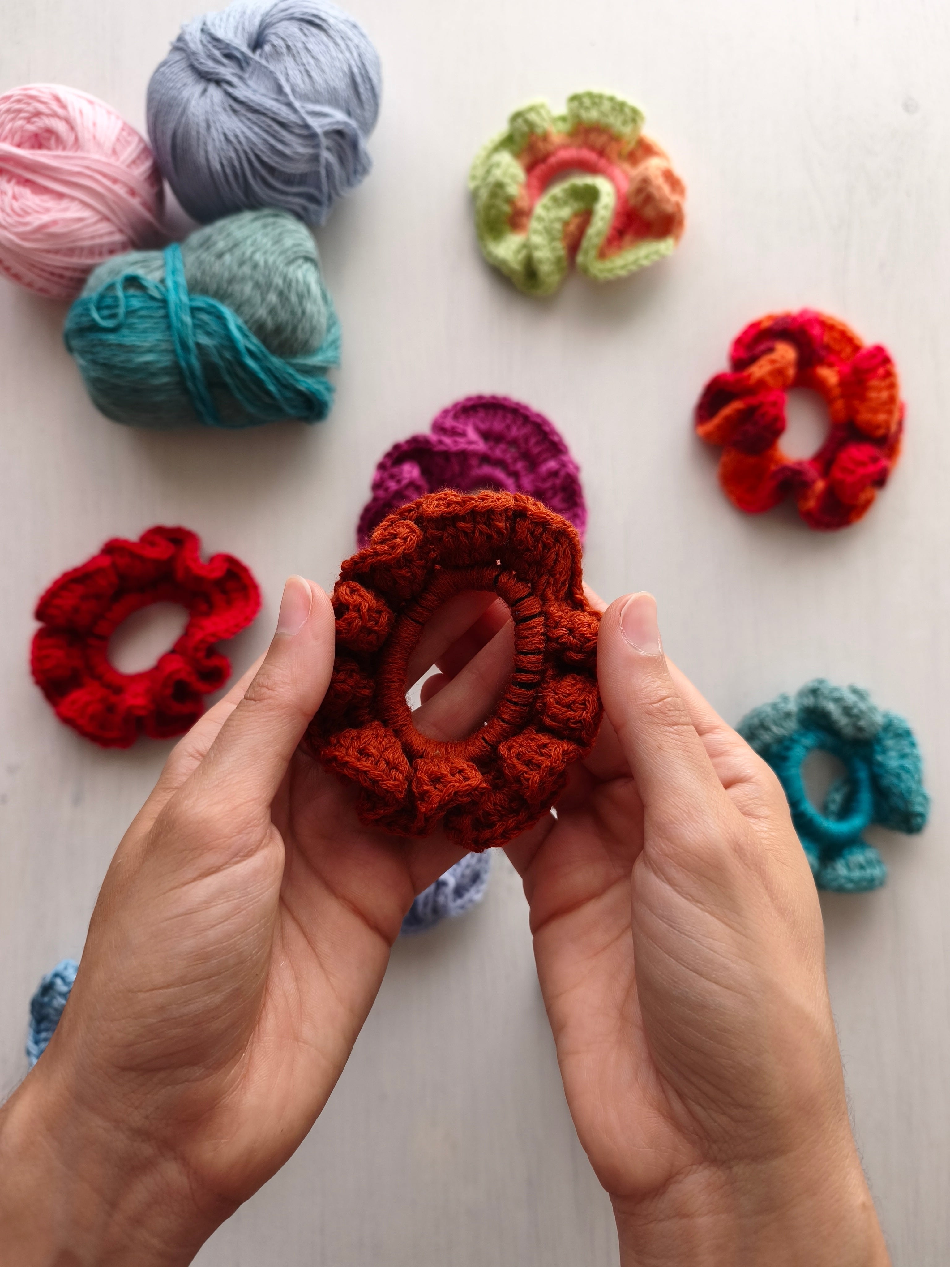 Mani che tengono uno scrunchie all'uncinetto arancione scuro