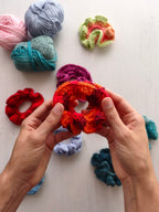 Mani che tengono uno scrunchie all'uncinetto arancione e rosso