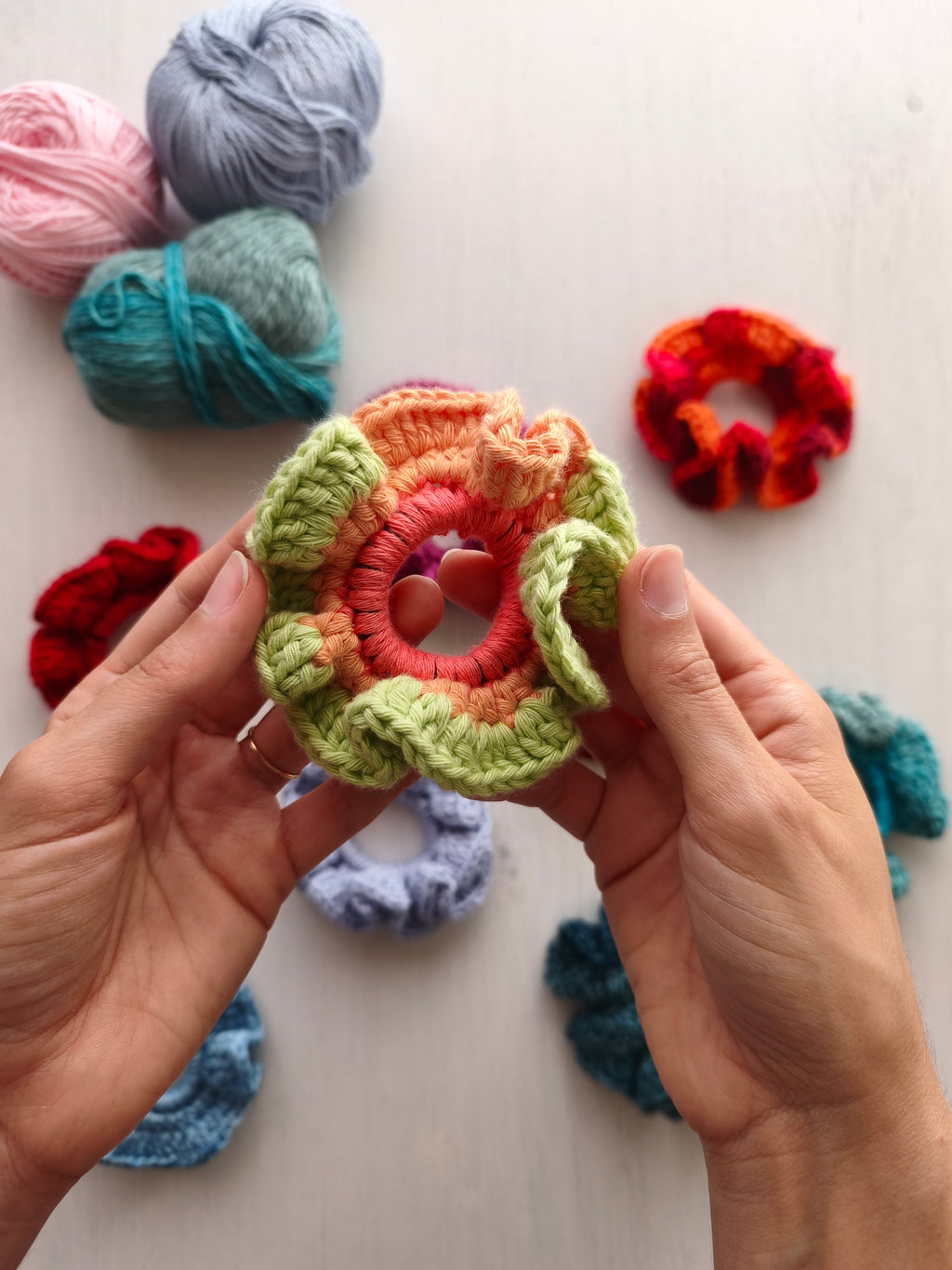 Mani che tengono uno scrunchie all'uncinetto corallo, arancio tenue e verde chiaro
