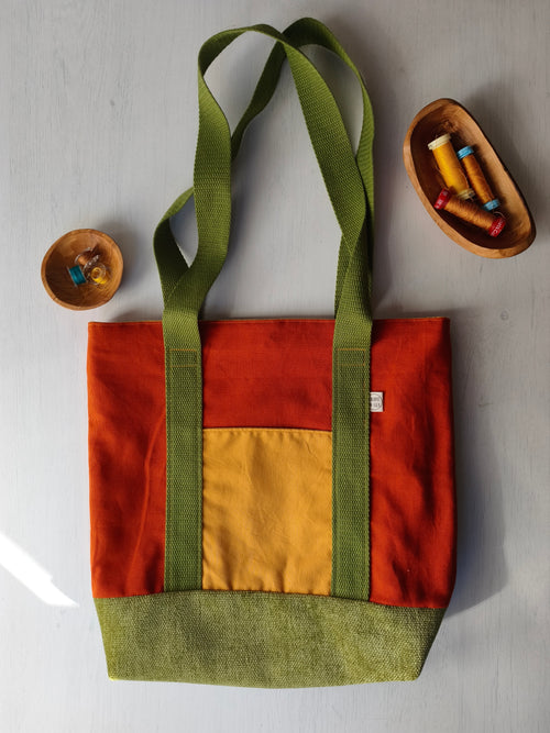 Borsa shopper arancione scuro con tasca esterna gialla, base verde e cinghie verdi