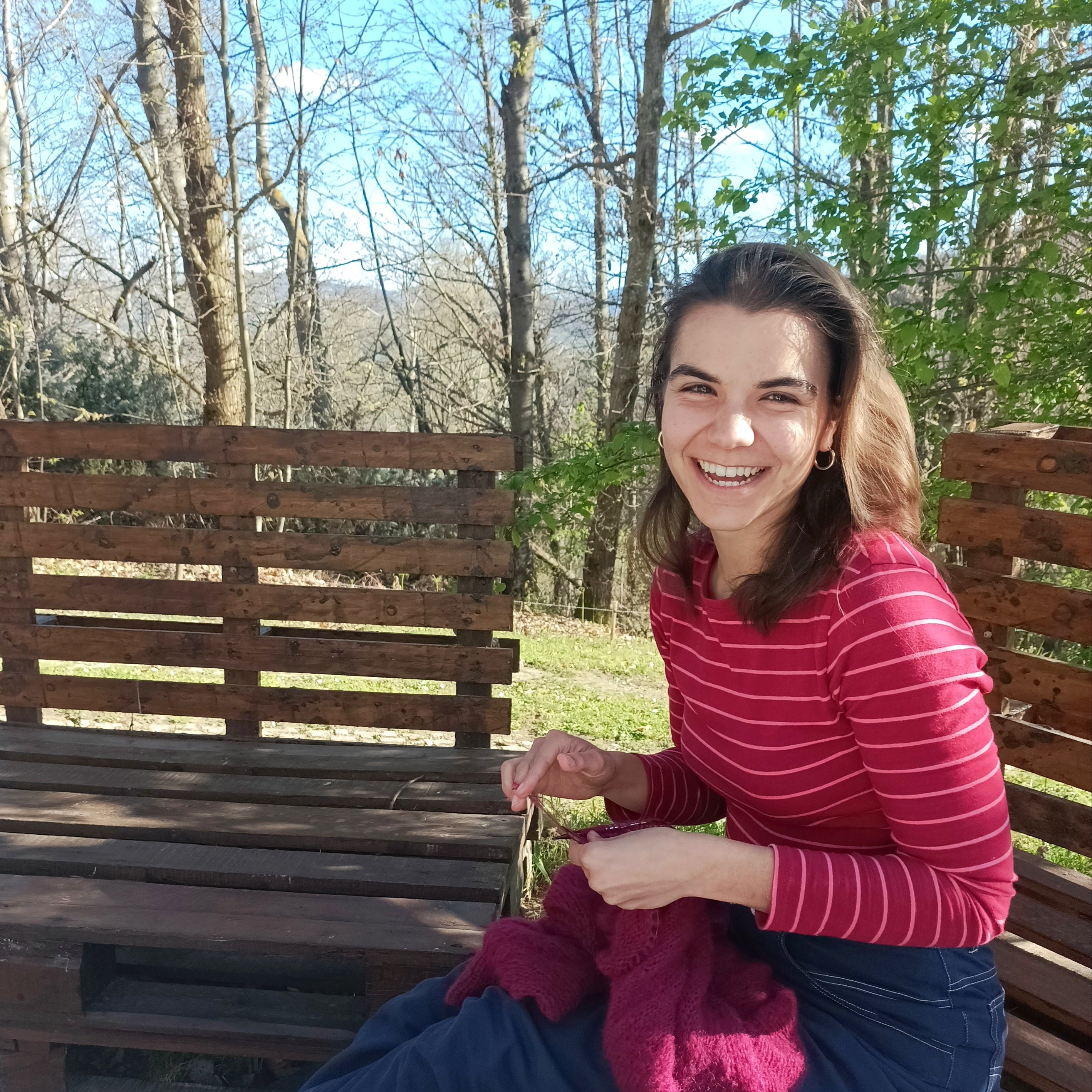 Gea lavora a maglia seduta su una panchina creata con dei pallet in un  contesto naturale